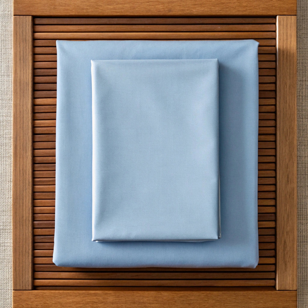 Overhead view of neatly folded dusty blue bamboo pillowcase with visible twill texture, placed on matching sheet or walnut nightstand