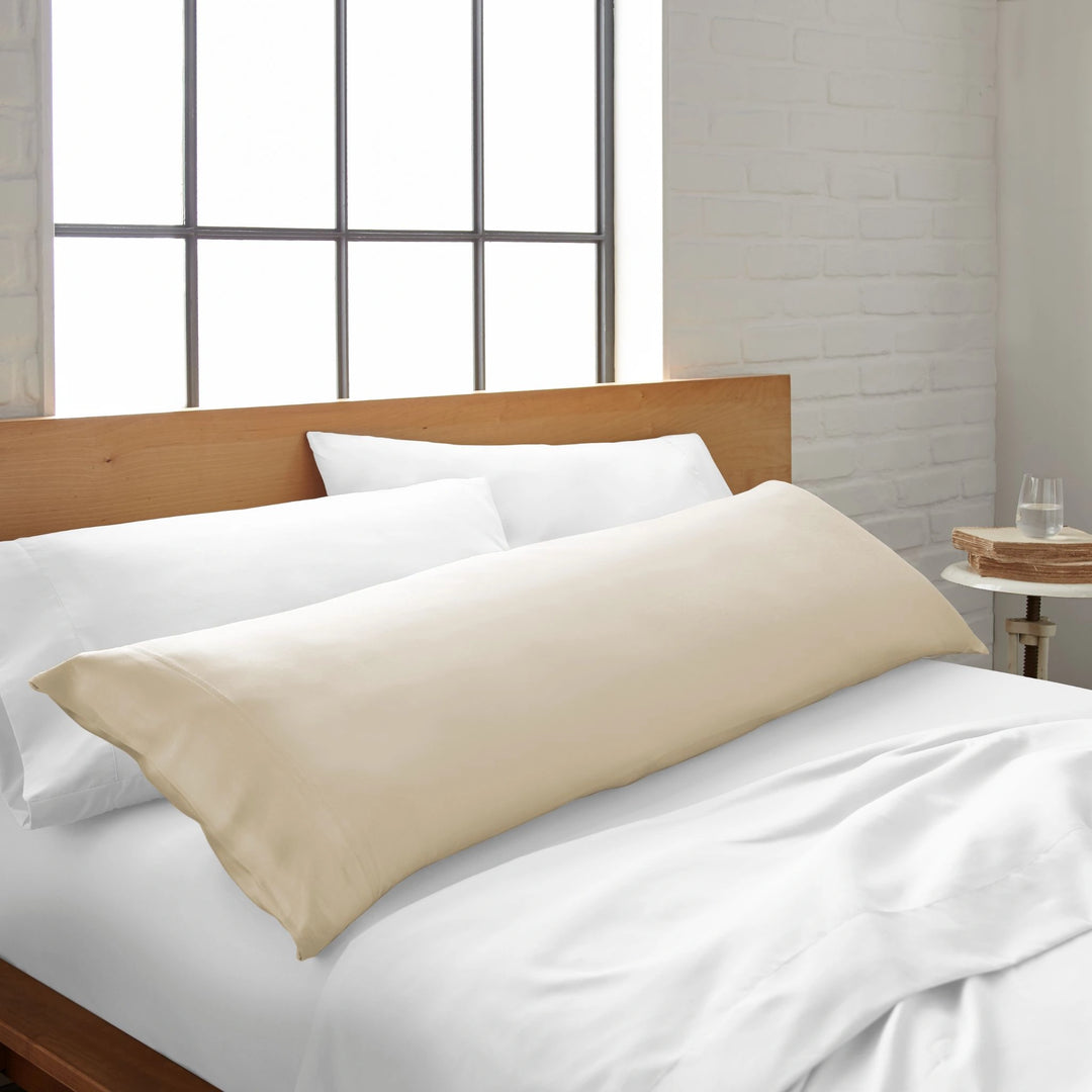 ivory bamboo body pillow from the Signature Collection, shown on a white bed in a bright modern bedroom with natural light and wood headboard
