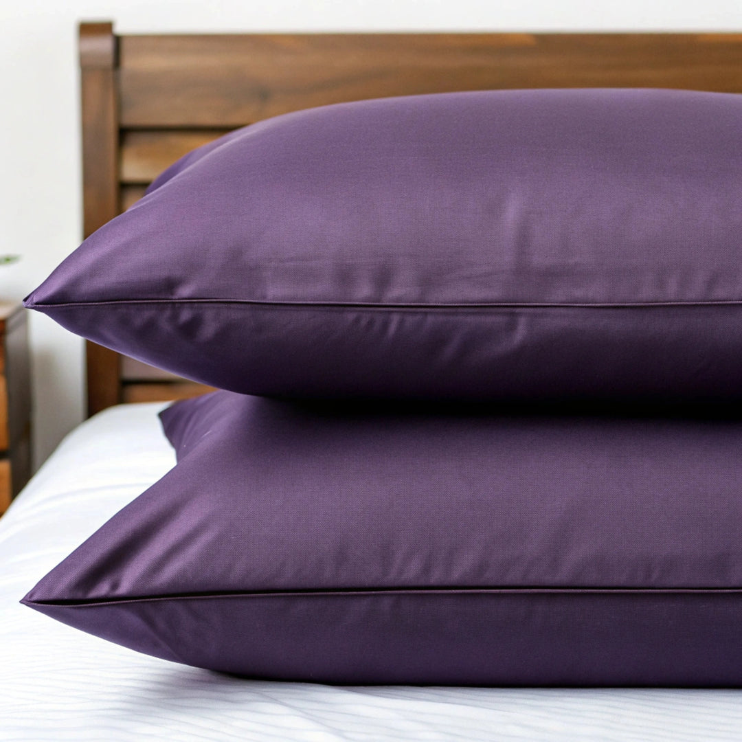 Close-up of two king-size pillows stacked neatly, dressed in matching royal purple bamboo pillowcases with a smooth twill weave and soft matte finish. The top pillow is slightly angled to showcase the fullness and plush texture, with no visible seams or stitching. Natural light highlights gentle fabric folds against a softly blurred walnut bed frame or clean white background, emphasizing the refined, breathable quality.