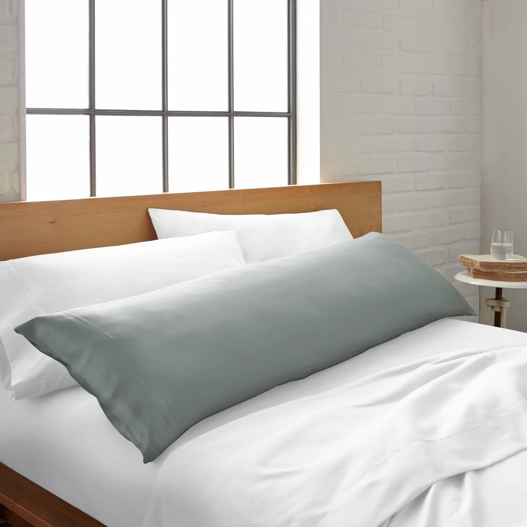 silver bamboo body pillow from the Signature Collection, shown on a white bed in a bright modern bedroom with natural light and wood headboard
