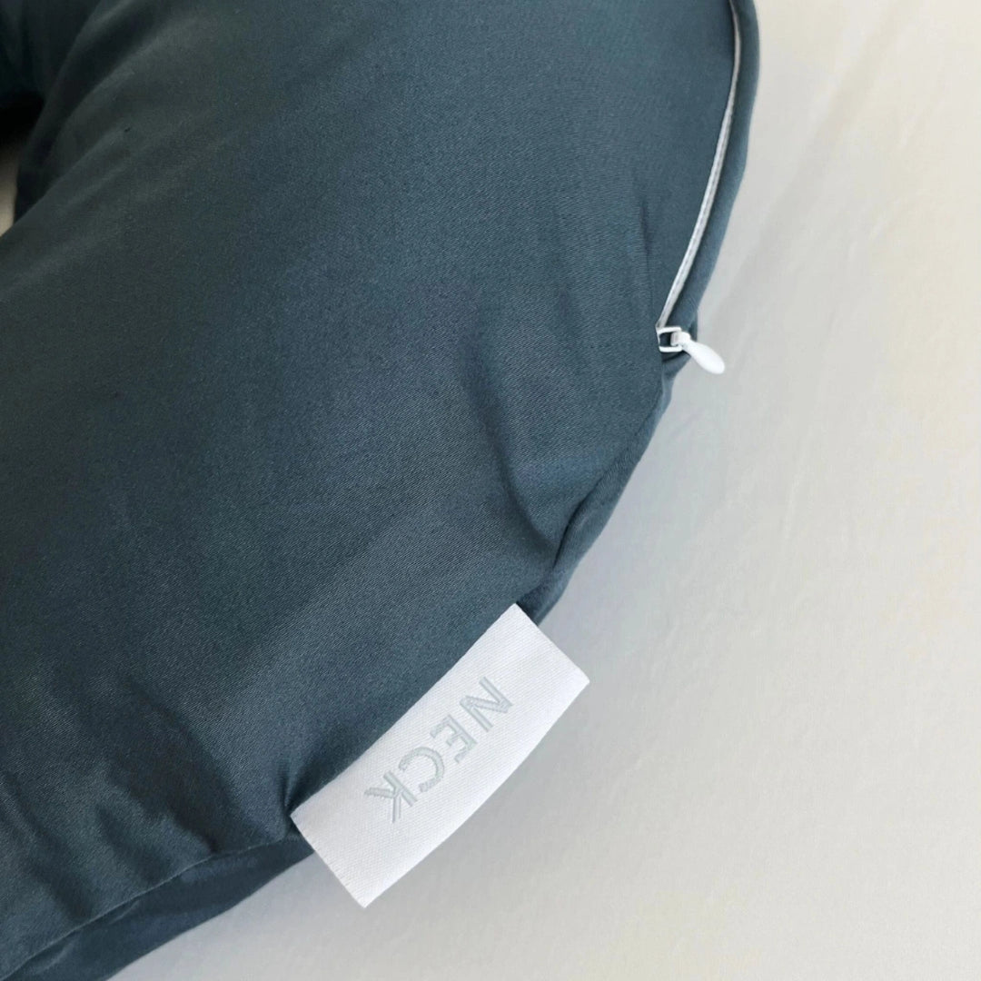 Slate blue travel pillow with visible brand tag stitched onto the side for identification and style detail