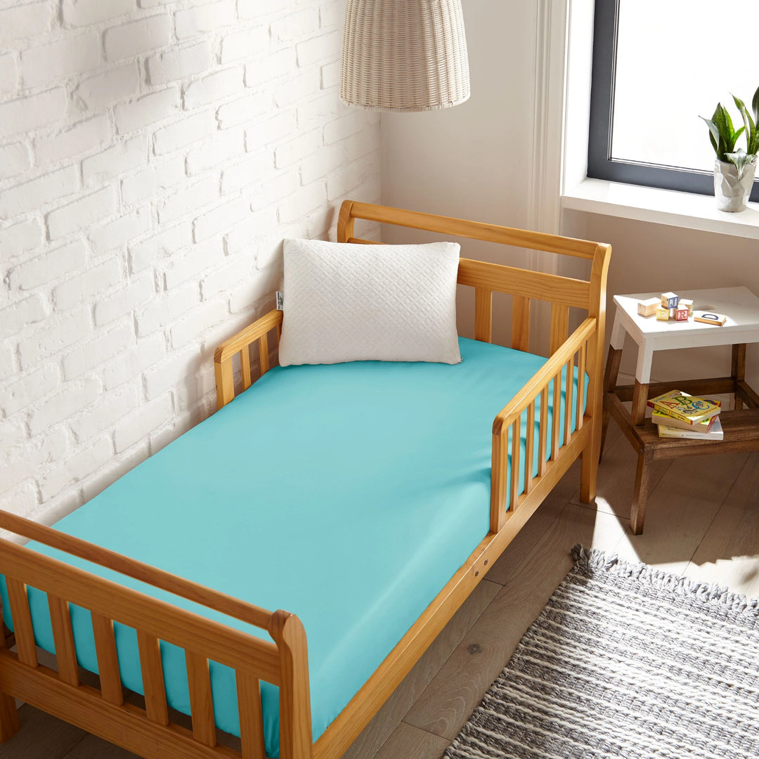 tiffany blue bamboo toddler fitted sheet from the Signature Collection, viewed from above on a light wood frame toddler bed in a bright modern nursery