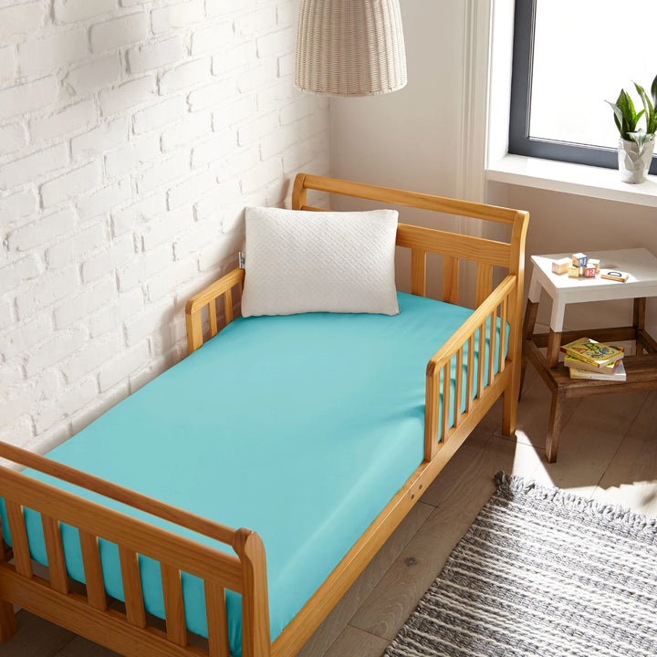 tiffany blue bamboo toddler fitted sheet from the Signature Collection, viewed from above on a light wood frame toddler bed in a bright modern nursery
