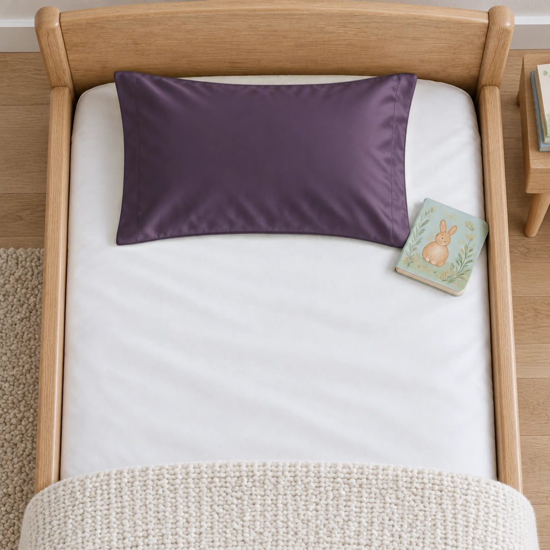 Overhead view of a royal purple bamboo viscose toddler pillowcase on a toddler bed, with a board book for scale