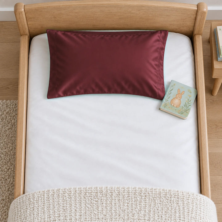 Overhead view of a ruby red bamboo viscose toddler pillowcase on a toddler bed, with a board book for scale