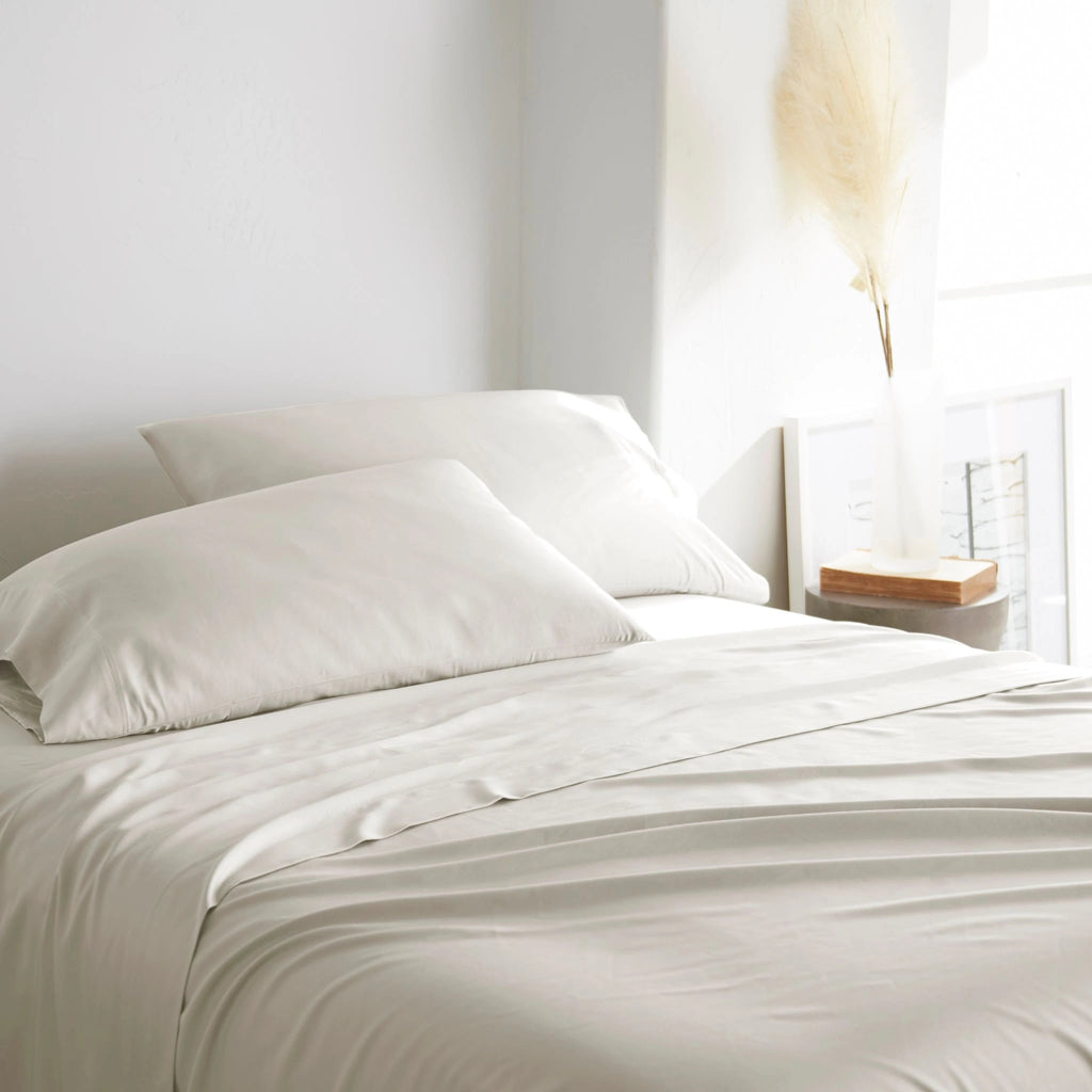 Cream bamboo bed sheets with sateen weave from the Premium Collection, three-quarter angle showing natural folds and soft lighting from nearby window