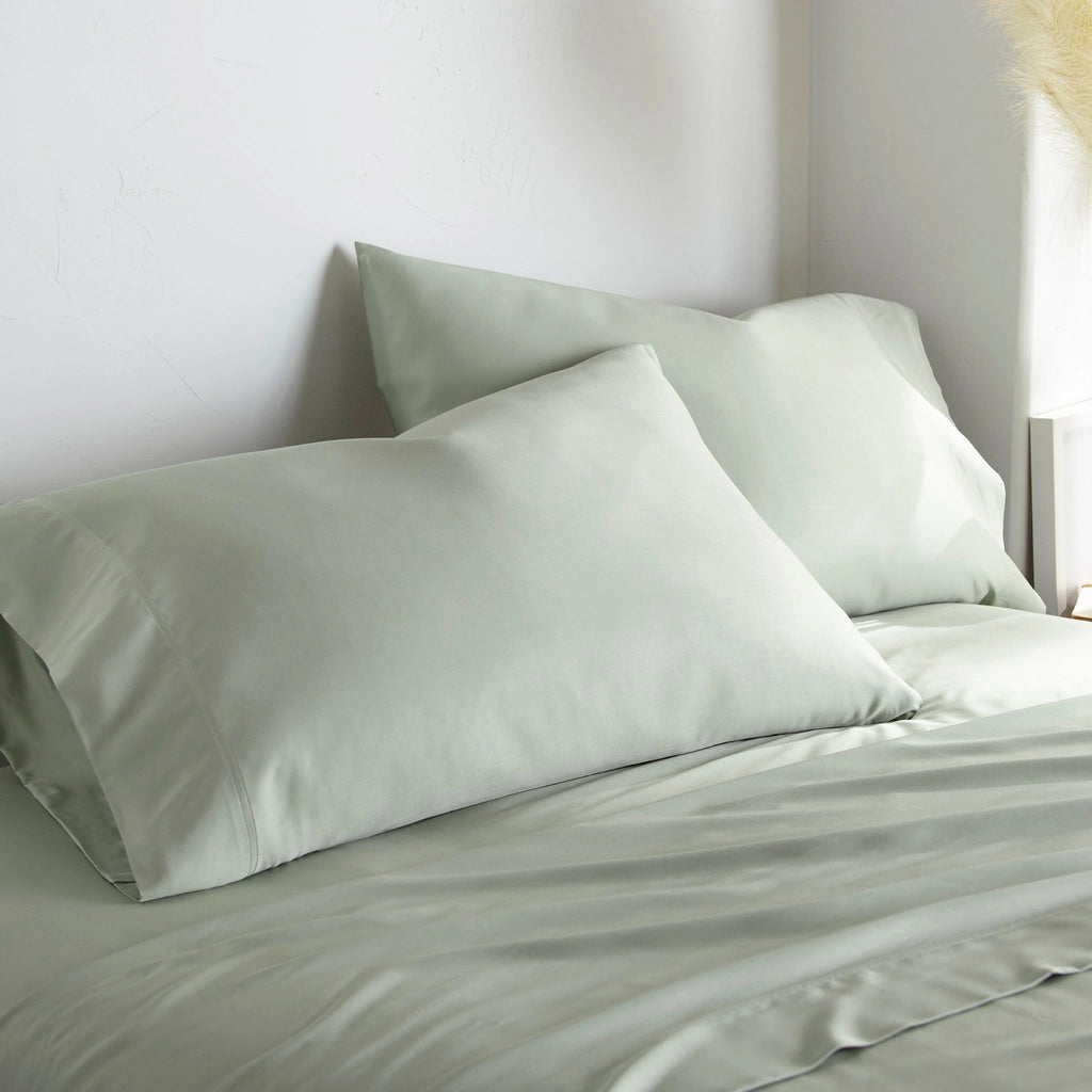 Sage bamboo bed sheets with sateen weave from the Premium Collection, three-quarter angle showing natural folds and soft lighting from nearby window
