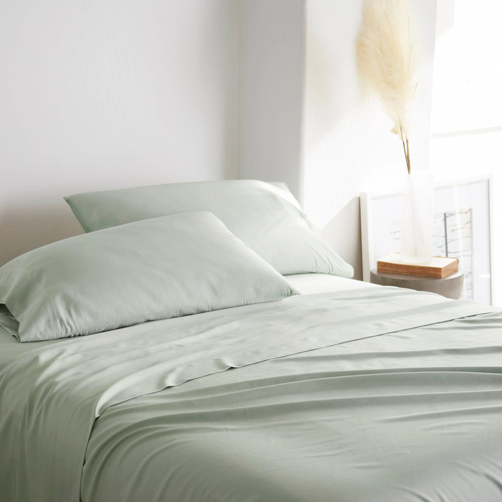 Sage bamboo bed sheets with sateen weave from the Premium Collection, three-quarter angle showing natural folds and soft lighting from nearby window