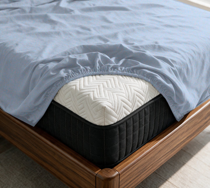 Dusty Blue copper-infused bamboo fitted sheet on a mattress in a sunlit walnut bedroom — breathable, cooling sateen weave.