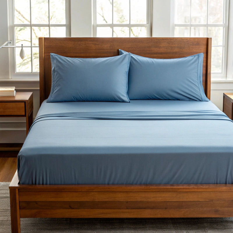 Front-facing view of a queen bed with dusty blue bamboo sheets and pillowcases, styled with a sateen finish and deep pocket fit.