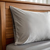 Feather gray bamboo pillowcase with smooth texture on a wood-frame bed, styled with soft natural light. Breathable and designed for cooler sleep.
