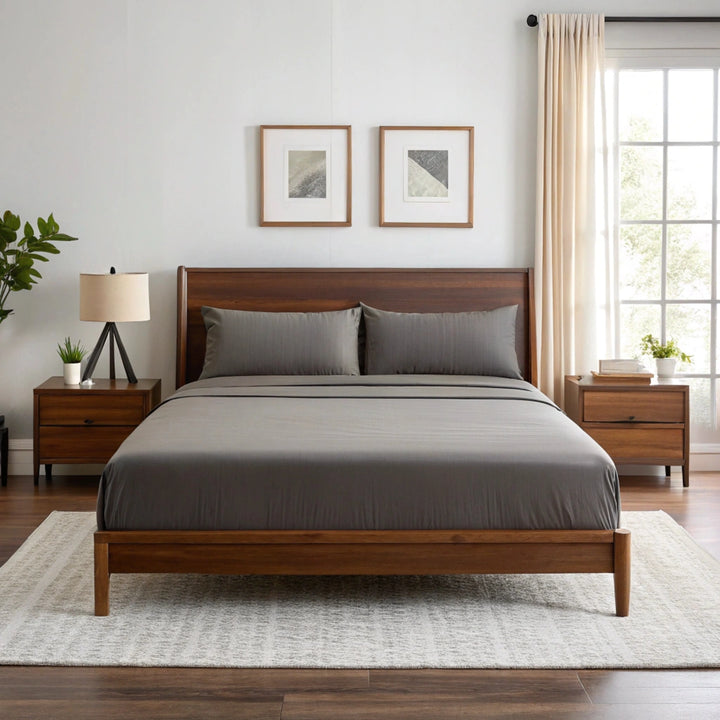 Wide-angle view of bedroom with feather gray bamboo sheets on walnut bed frame, featuring matching nightstand, ceramic lamp, glass vase with greenery, soft rug, and minimal wall art.