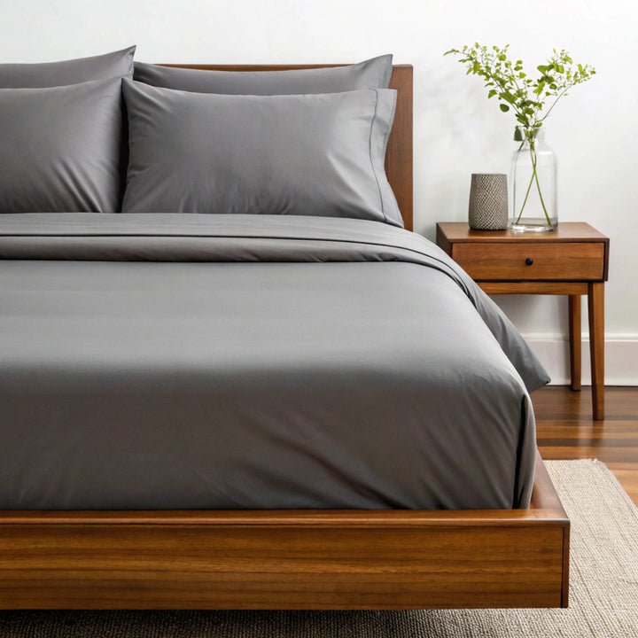 Side angle shot from pillow-end showing feather gray  bamboo pillowcases and sheet set with decorative plant and soft lighting.
