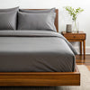 Side angle shot from pillow-end showing feather gray  bamboo pillowcases and sheet set with decorative plant and soft lighting.