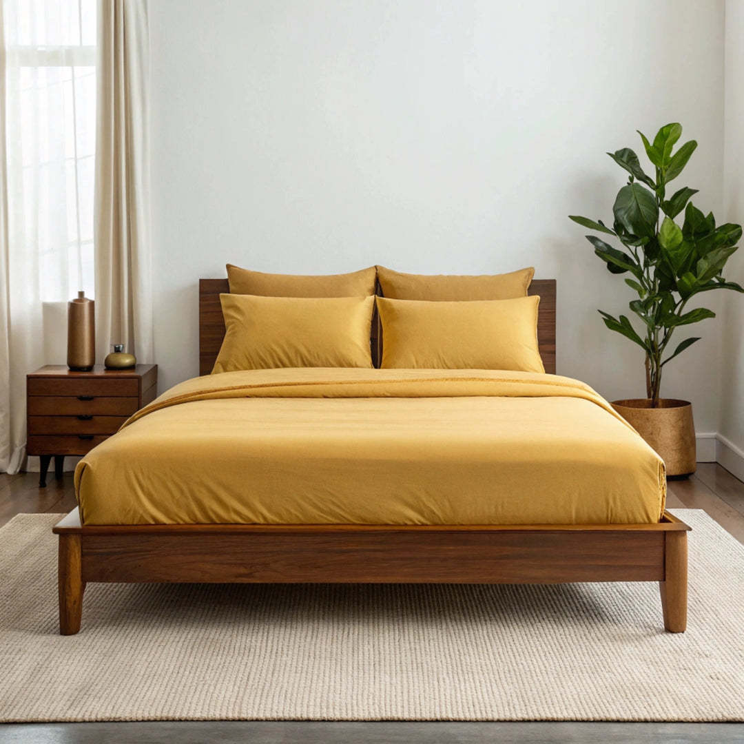 Wide-angle view of bedroom with graphite gray bamboo sheets on walnut bed frame, featuring matching nightstand, ceramic lamp, glass vase with greenery, soft rug, and minimal wall art.