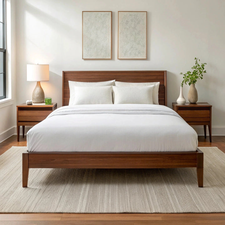 Wide-angle view of bedroom with powder white bamboo sheets on walnut bed frame, featuring matching nightstand, ceramic lamp, glass vase with greenery, soft rug, and minimal wall art