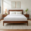 Wide-angle view of bedroom with powder white bamboo sheets on walnut bed frame, featuring matching nightstand, ceramic lamp, glass vase with greenery, soft rug, and minimal wall art