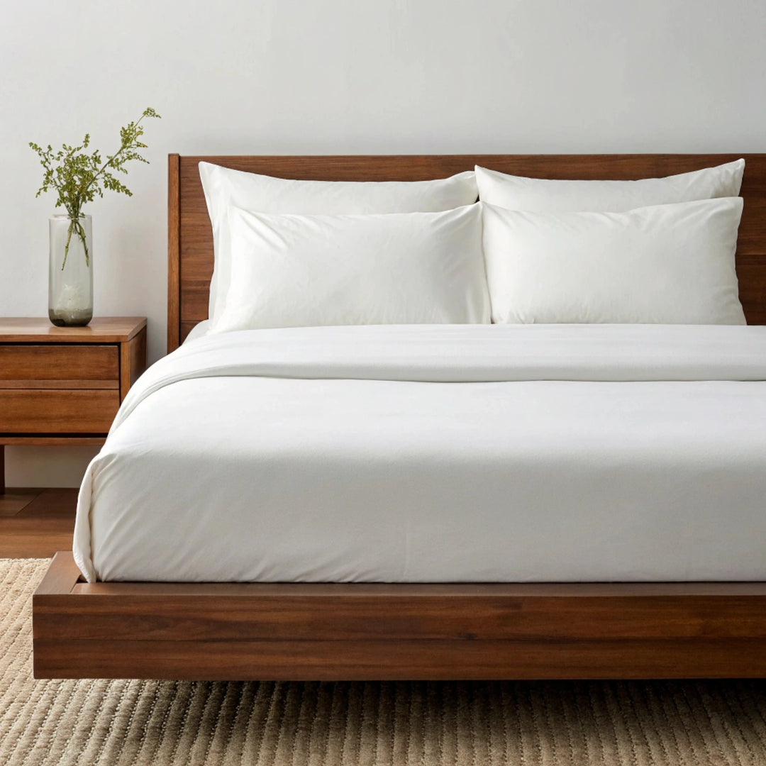 Side angle shot from pillow-end showing powder white bamboo pillowcases and sheet set with decorative plant and soft lighting.