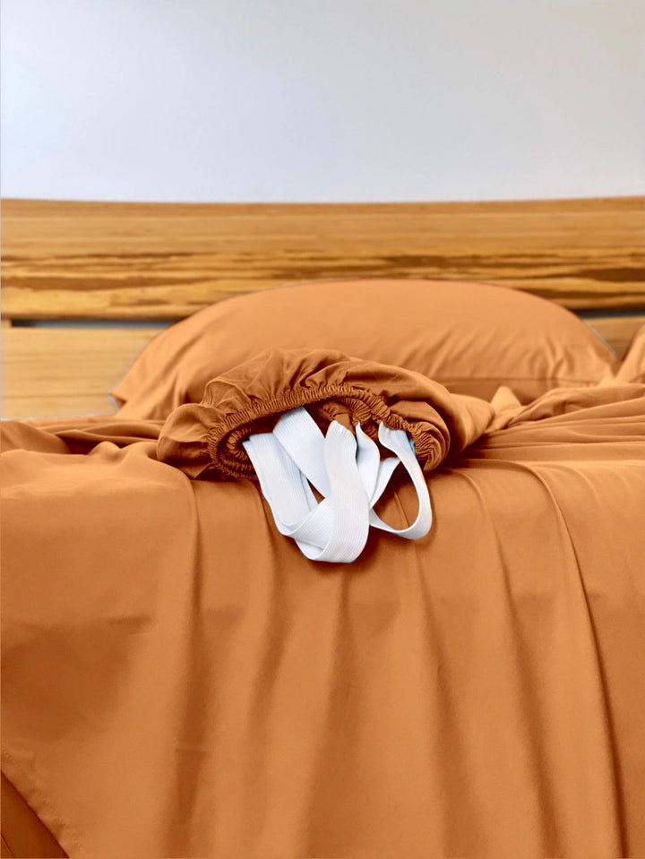 Rust copper-infused bamboo fitted sheet — corner detail showing the elastic hem and reinforced corner straps for a secure fit.