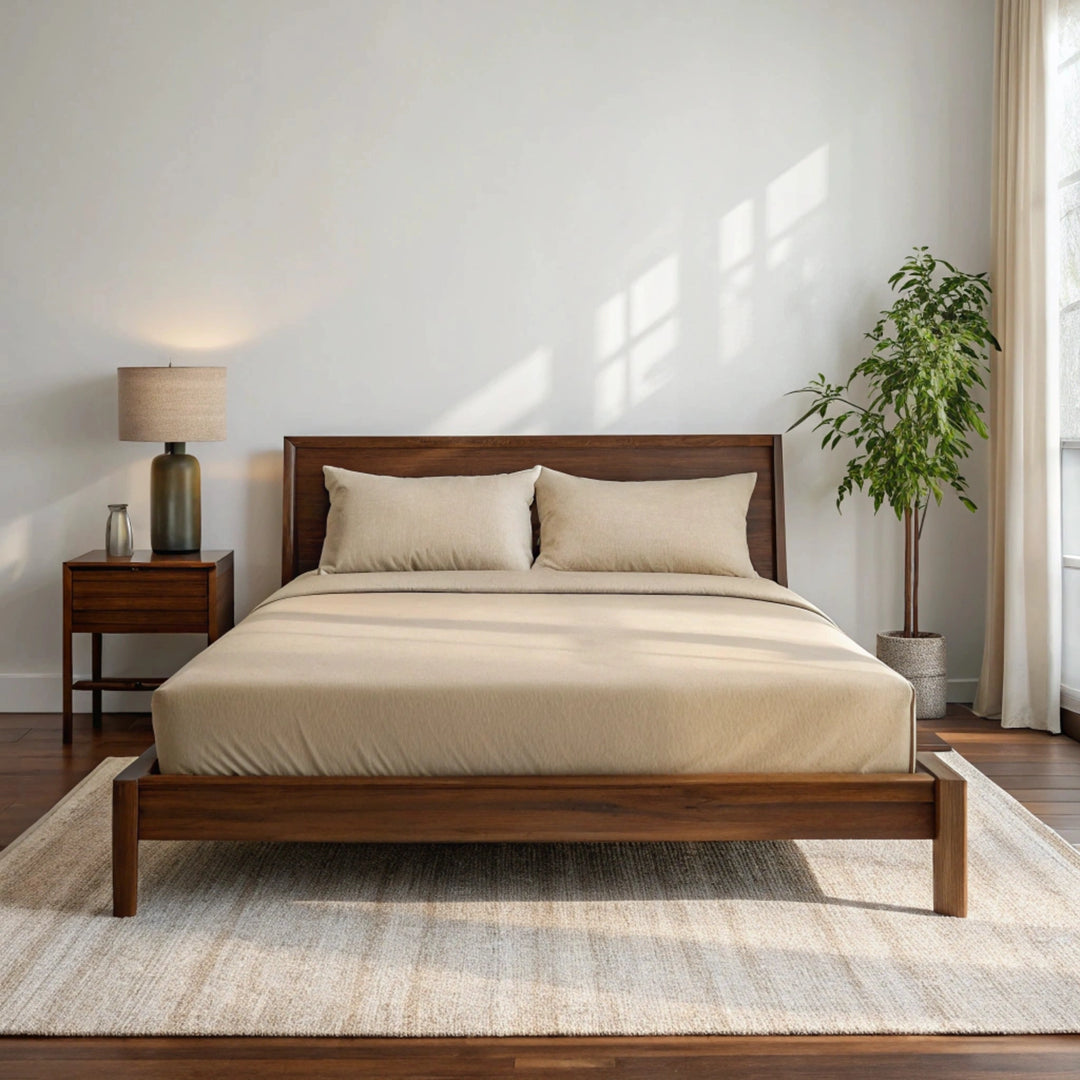 Wide-angle view of bedroom with summer sand bamboo sheets on walnut bed frame, featuring matching nightstand, ceramic lamp, glass vase with greenery, soft rug, and minimal wall art.