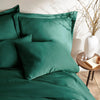close-up of emerald green bamboo sateen pillowcases and duvet cover on king bed, styled against a textured cream wall with natural decor
