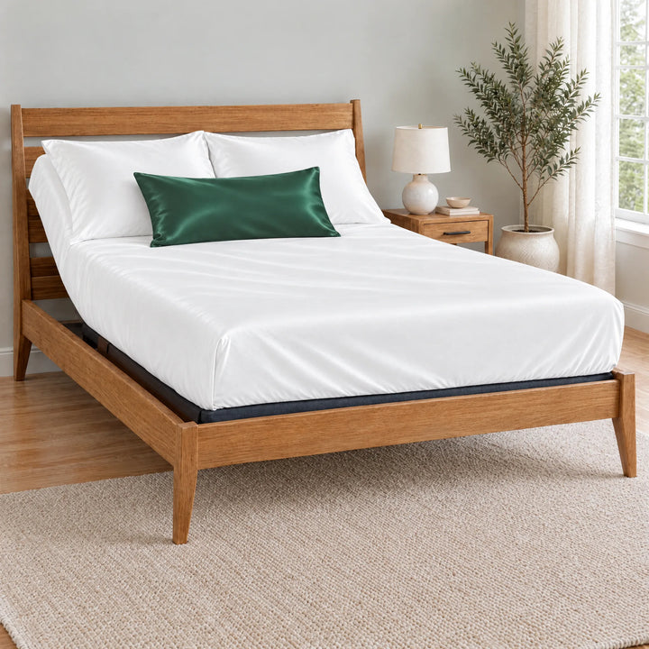 Emerald Green bamboo viscose sateen lumbar pillowcase on a made bed in front of white pillows in a light oak bedroom with an olive tree