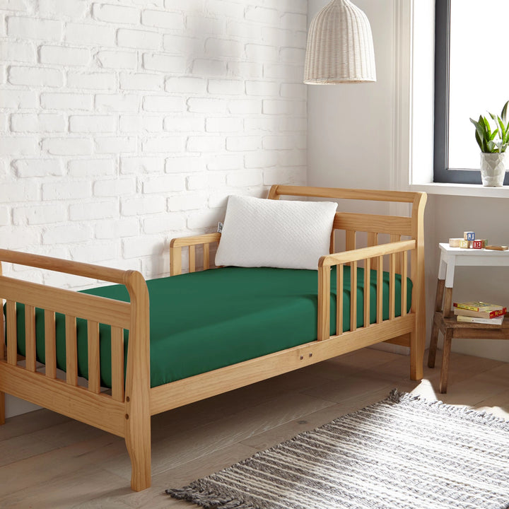 emerald green bamboo toddler fitted sheet from the Signature Collection, styled in a wooden toddler bed with emerald green pillow and modern nursery decor
