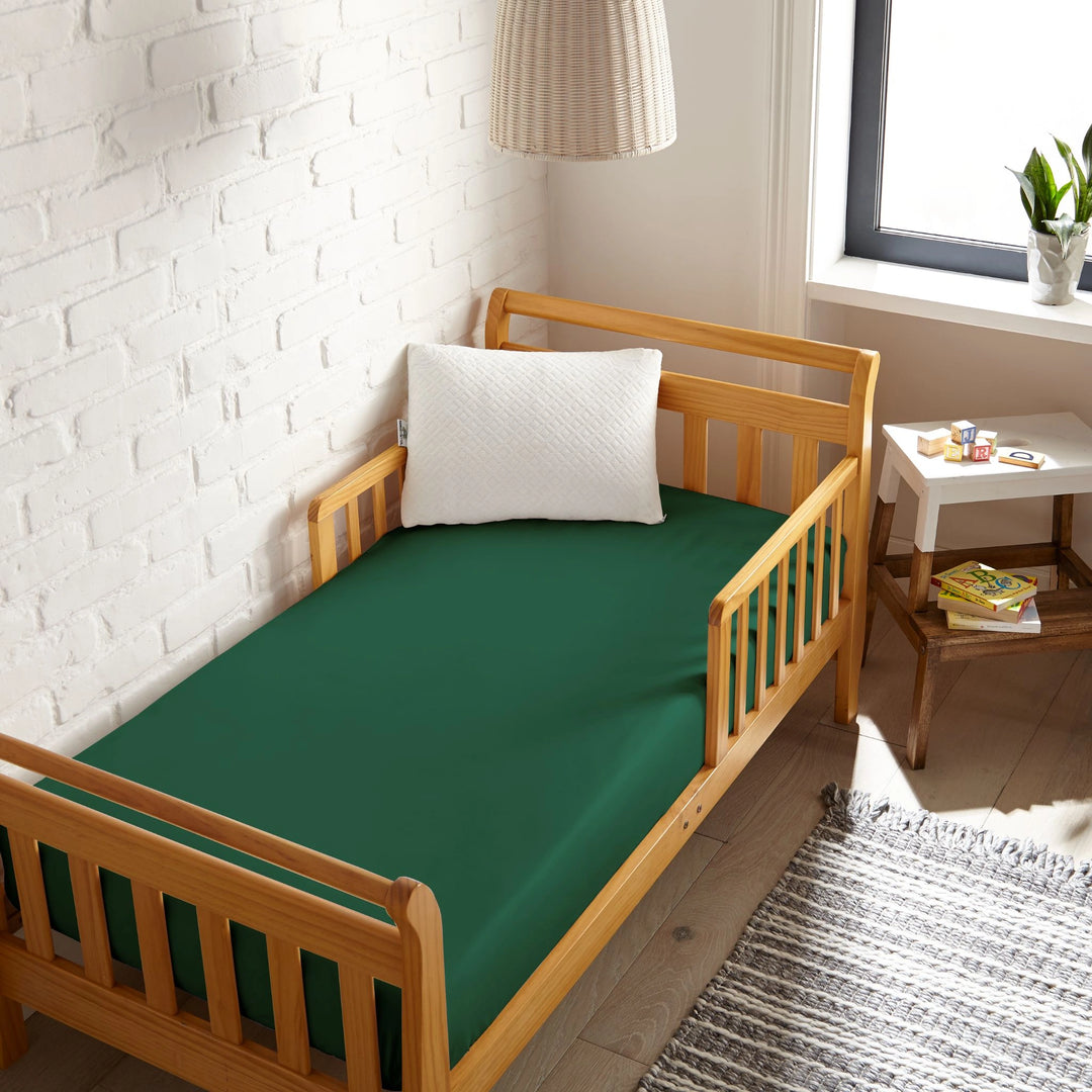 emerald green bamboo toddler fitted sheet from the Signature Collection, viewed from above on a light wood frame toddler bed in a bright modern nursery