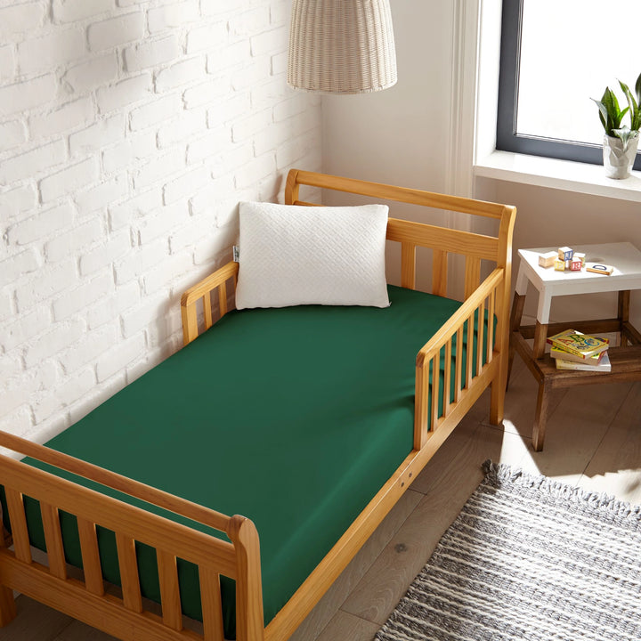 emerald green bamboo toddler fitted sheet from the Signature Collection, viewed from above on a light wood frame toddler bed in a bright modern nursery