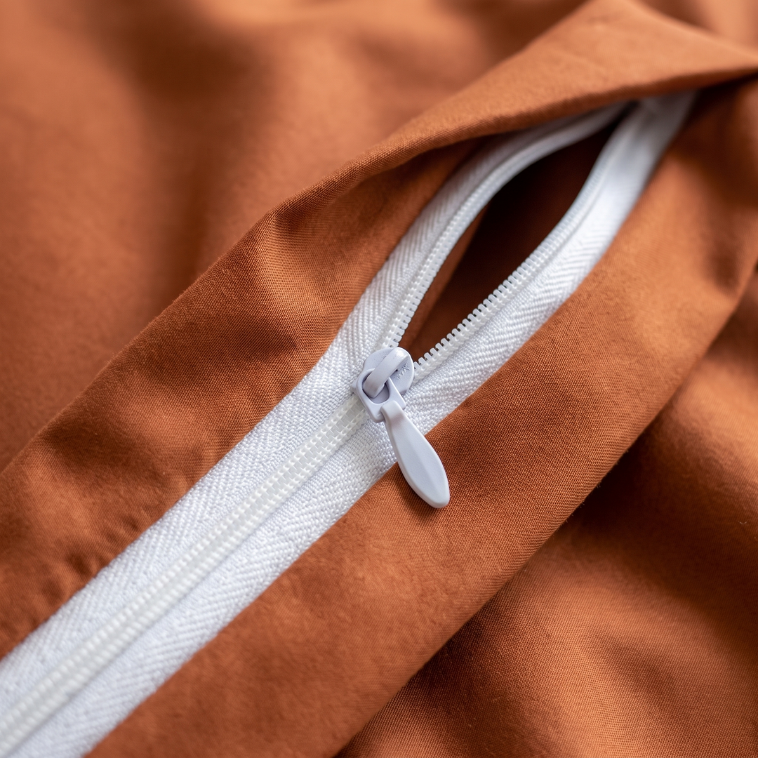 Rust copper-infused bamboo viscose duvet cover, close-up of the zipper closure at the foot of the cover, white coil zipper with a molded plastic pull tab.