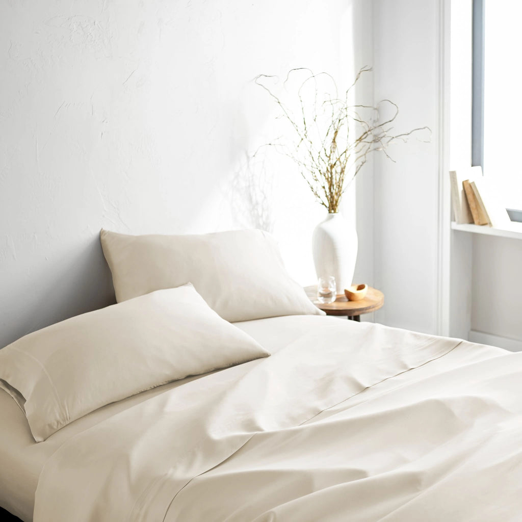 ivory bamboo bed sheets with sateen weave from the Signature Collection, three-quarter angle showing natural folds and soft lighting from nearby window