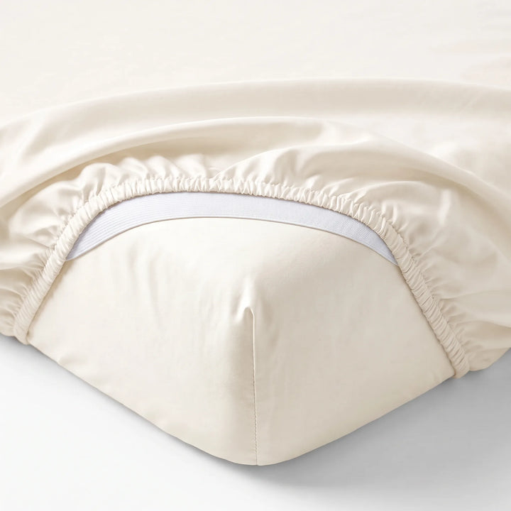 ivory bamboo sateen fitted sheet corner with white elastic strap, showing snug fit and smooth fabric texture