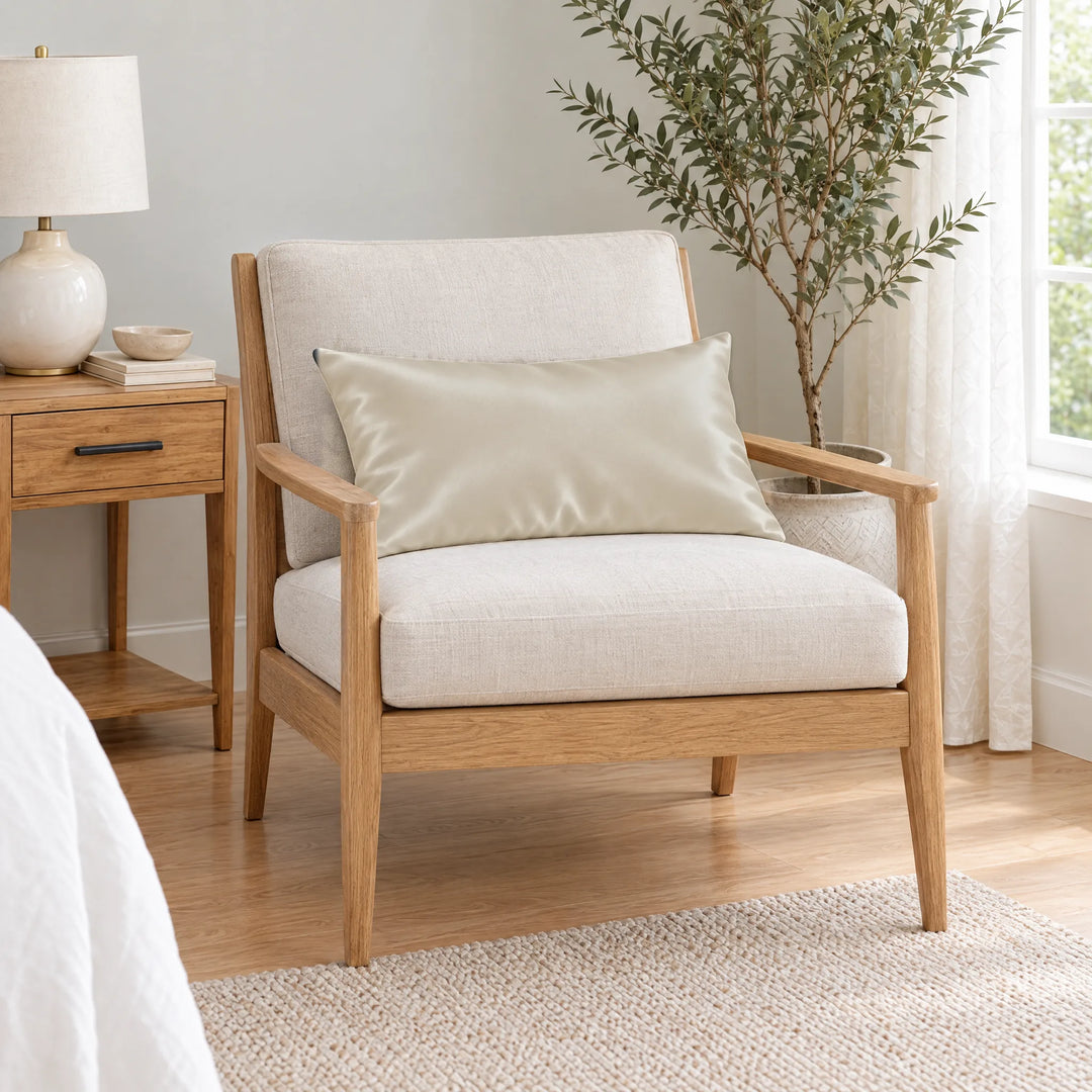 Ivory bamboo viscose sateen lumbar pillowcase on a light oak armchair beside a nightstand and olive tree