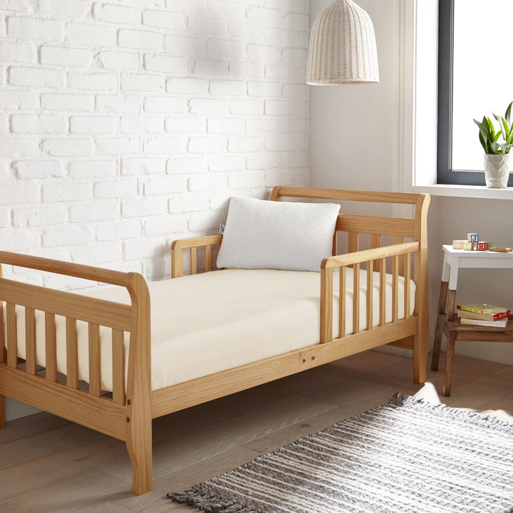 ivory bamboo toddler fitted sheet from the Signature Collection, styled in a wooden toddler bed with white pillow and modern nursery decor