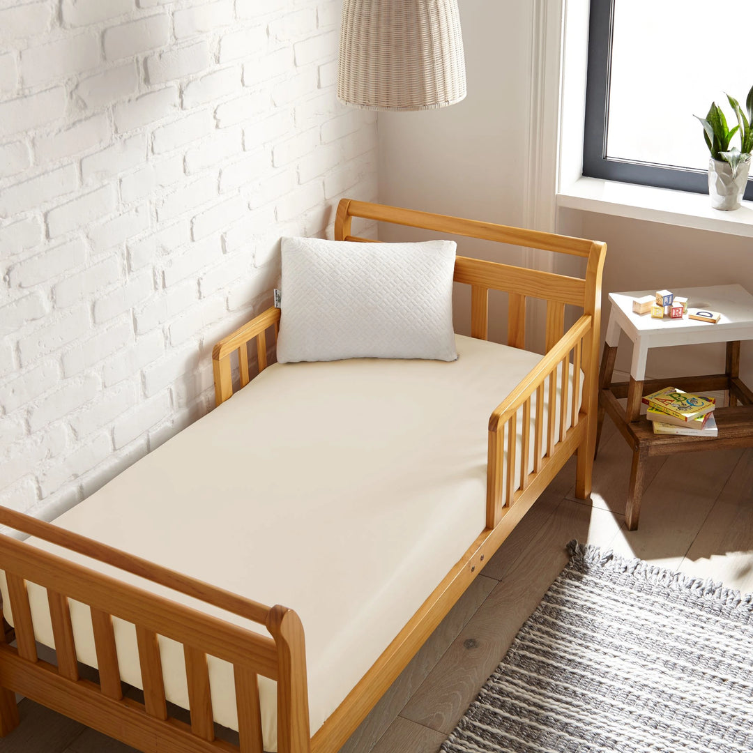 ivory bamboo toddler fitted sheet from the Signature Collection, viewed from above on a light wood frame toddler bed in a bright modern nursery