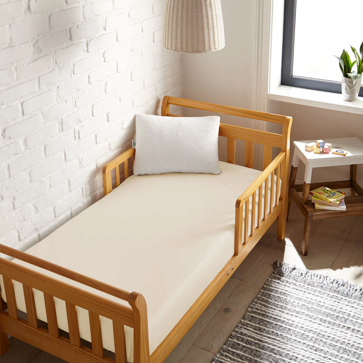 ivory bamboo toddler fitted sheet from the Signature Collection, viewed from above on a light wood frame toddler bed in a bright modern nursery