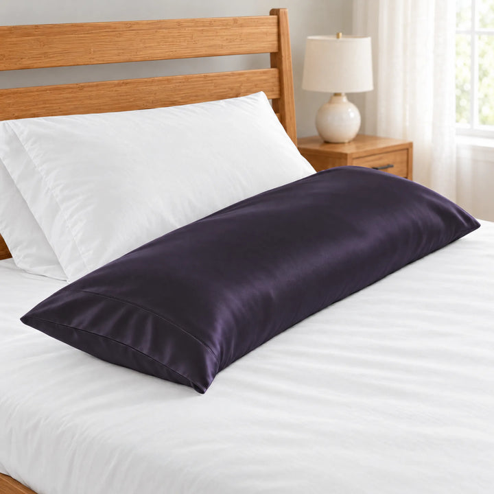 Royal Purple bamboo viscose sateen body pillowcase close-up of the stitched hem beside a white pillow on a made bed, honey bamboo headboard and lamp in soft focus