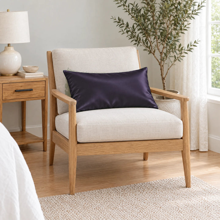 Royal Purple bamboo viscose sateen lumbar pillowcase on a light oak armchair beside a nightstand and olive tree