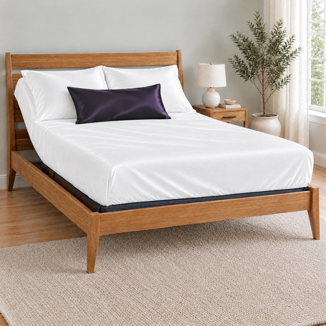 Royal Purple bamboo viscose sateen lumbar pillowcase on a made bed in front of white pillows in a light oak bedroom with an olive tree