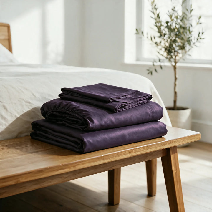 royal purple bamboo viscose sheet set folded on a bamboo bench: flat sheet, fitted sheet and pillowcases
