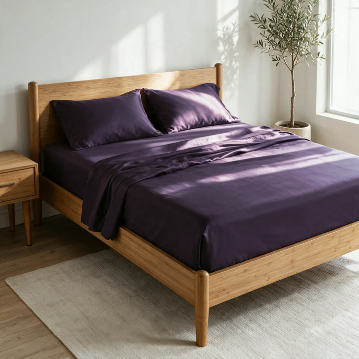 royal purple bamboo viscose sateen sheet set on a caramelized bamboo bed frame in a bright bedroom with a cream rug and olive tree