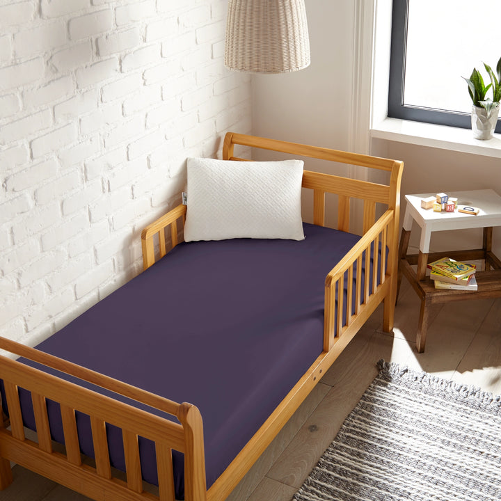 royal purple bamboo toddler fitted sheet from the Signature Collection, viewed from above on a light wood frame toddler bed in a bright modern nursery