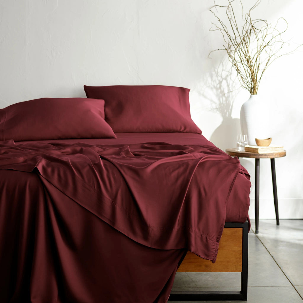 ruby red bamboo bed sheets with sateen weave from the Signature Collection, shown from the foot of the bed with a draped flat sheet and matching pillowcases