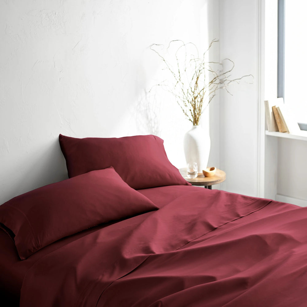 ruby red bamboo bed sheets with sateen weave from the Signature Collection, three-quarter angle showing natural folds and soft lighting from nearby window
