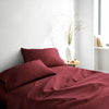 ruby red bamboo bed sheets with sateen weave from the Signature Collection, three-quarter angle showing natural folds and soft lighting from nearby window