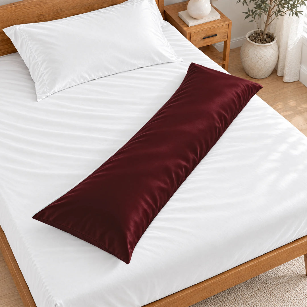 Ruby Red bamboo viscose sateen body pillowcase lying diagonally across a made bed, overhead view in a bright bedroom with a honey bamboo bed