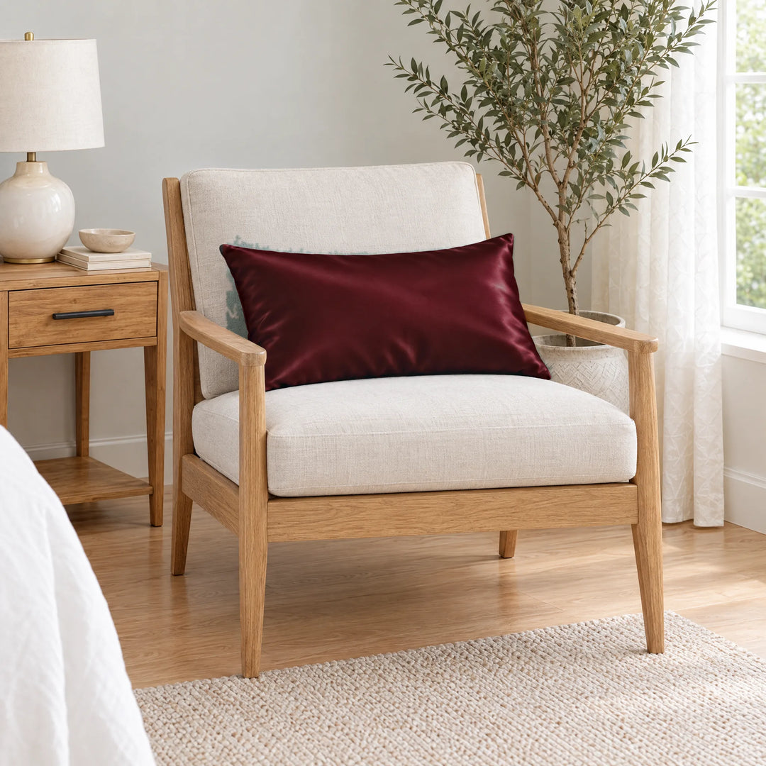 Ruby Red bamboo viscose sateen lumbar pillowcase on a light oak armchair beside a nightstand and olive tree