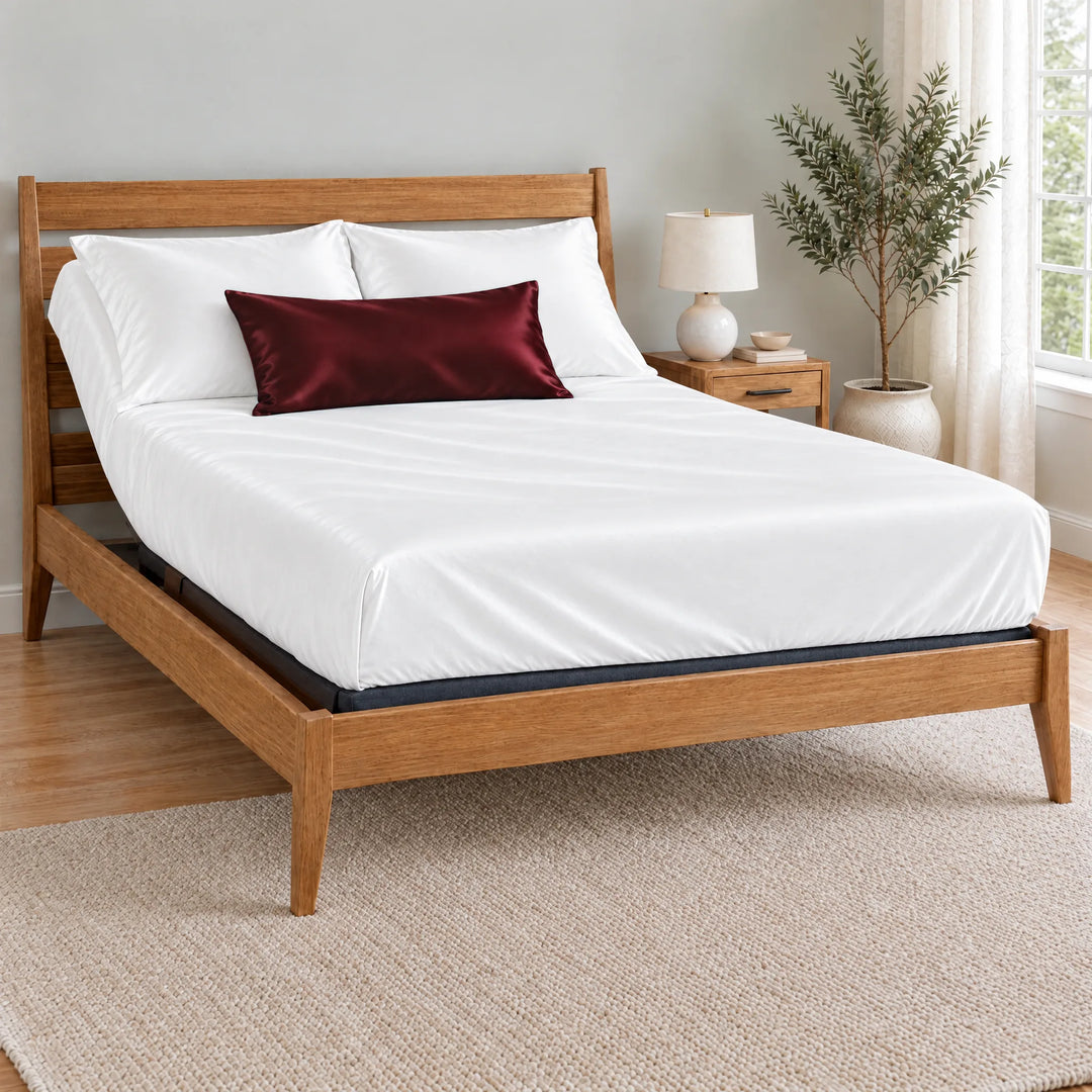 Ruby Red bamboo viscose sateen lumbar pillowcase on a made bed in front of white pillows in a light oak bedroom with an olive tree