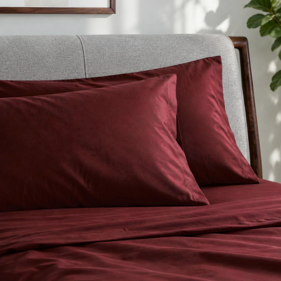 ruby red bamboo viscose sateen pillowcases against a light grey headboard, showing the seams and soft low-sheen finish