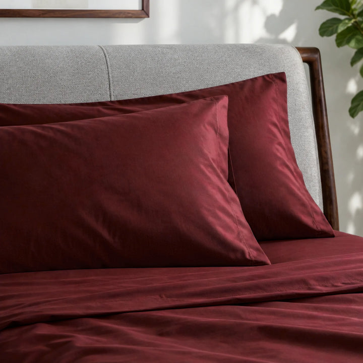 ruby red bamboo viscose sateen pillowcases against a light grey headboard, showing the seams and soft low-sheen finish